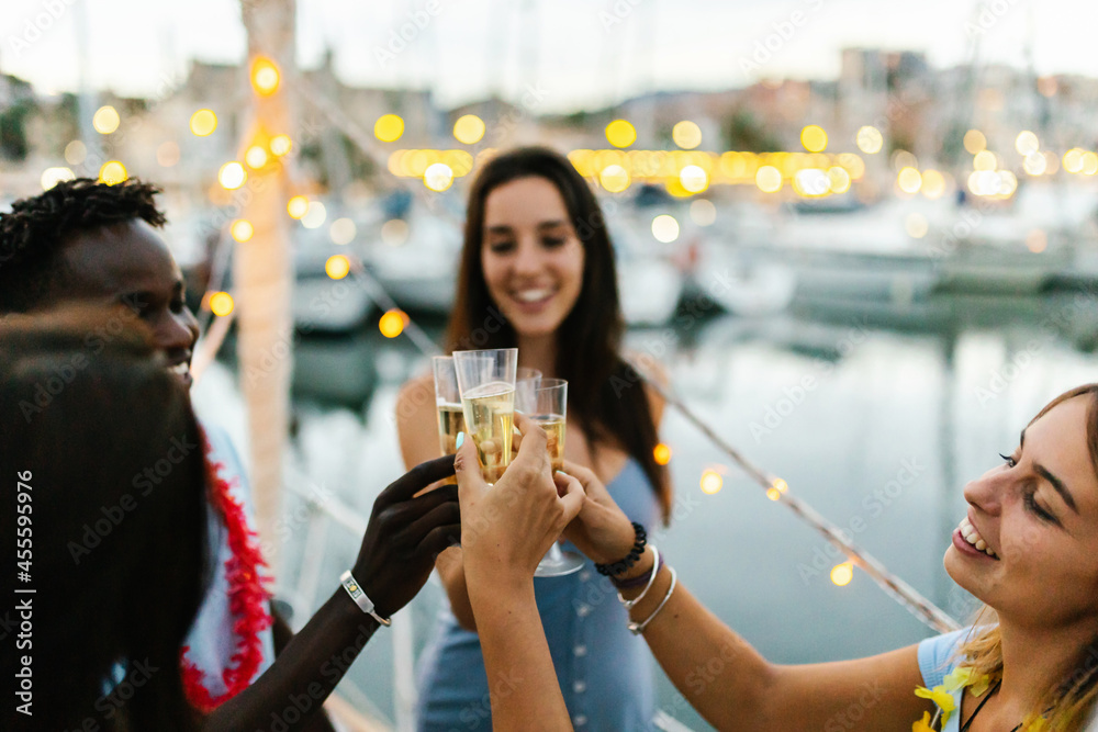 Happy multiracial young people cheering with champagne on a boat during christmas holidays - Millennial friends celebrate birthday together - Friendship, eve and celebration concept