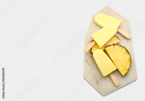 Board with tasty pineapple popsicle on white background