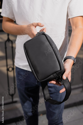 Man holding his new black leather banana bag in a city