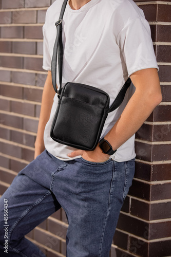 Cropped unrecognizable man holding his new black leather messenger bag leaning at wall