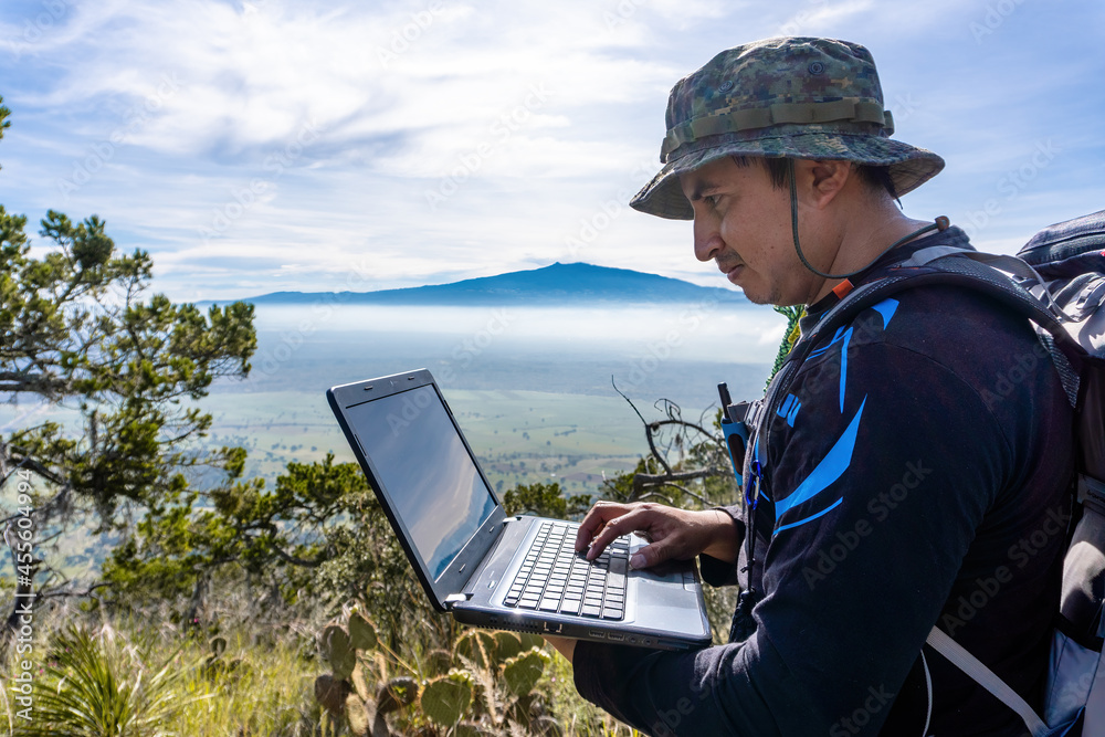 A portrait of a freelancer man with glasses with a laptop sitting on a rock in a mountain A portrait of a freelancer man with glasses with a laptop sitting on a rock in a mountain