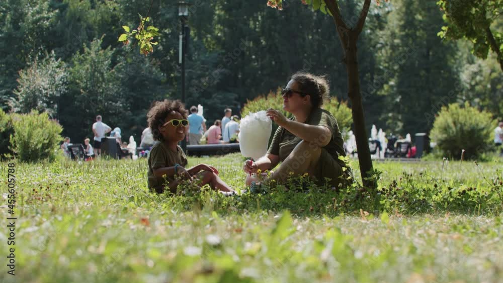 Mixed family of mother and daughter in sunglasses spending time in the park - eating cotton candy Mixed family of mother and daughter in sunglasses spending time in the park - eating cotton candy