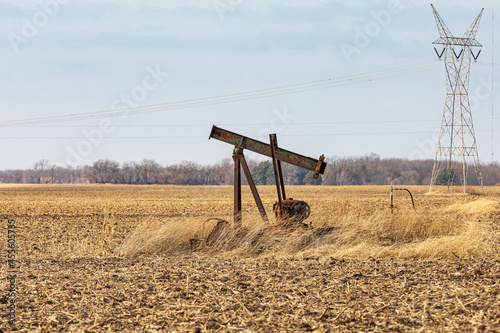 Old, orphaned oil well pump in farm field.  oil well abandonment, decommission, and oil production concept. photo