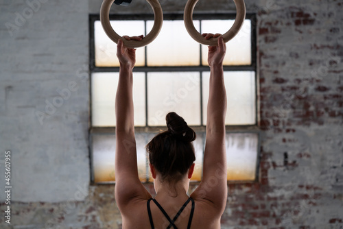 Back view of fit young caucasian woman in sports wear. Healthy young woman exercising with gymnastic rings. Female bodybuilder with power hand, triceps, arms, rear in gym