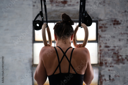 Back view of fit young caucasian woman in sports wear. Healthy young woman exercising with gymnastic rings. Female bodybuilder with power hand, triceps, arms, rear in gym