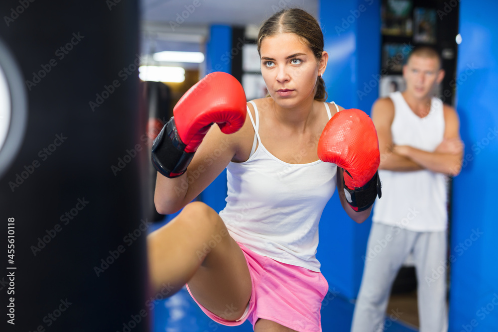 Young european boxer woman in boxing gloves is practicing different kicks at gym