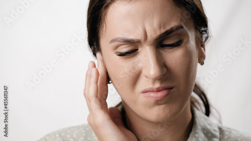 Earache. Suffering woman on white background with emotions of pain on her face touches her ear. Close-up photo