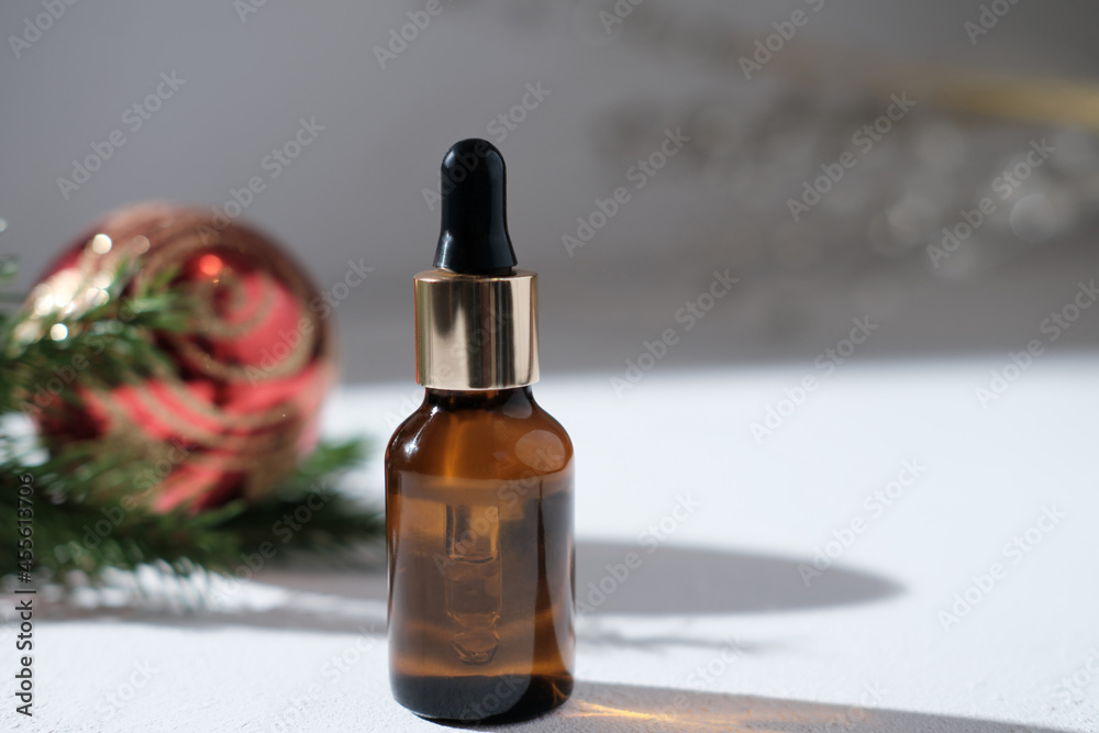 face care serum or oil in amber glass bottle with dropper next to christmas decor on a table. red christmas ball and pine branch. copy space. cosmetic seasonal sale.