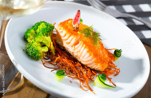 Appetizing roasted salmon steak on carrot brushwood with sauce and broccoli garnished with cucumber, figs and dill
