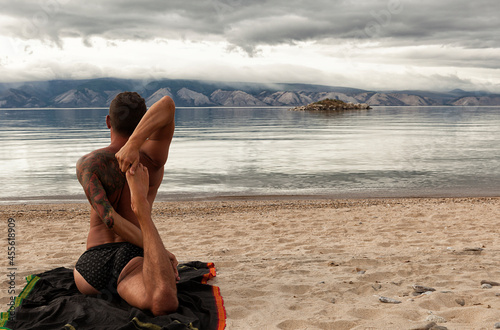 strong young man does yoga on the sandy shore of a mountain lake, yoga practice on the beach