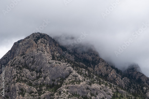 Rocky mountains with green spruce forest and misty clouds.. Nature landscape background. Komirshi gorge in Kazakhstan.