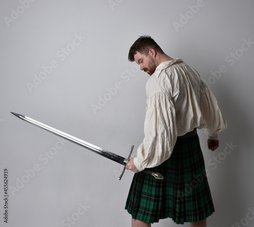 фотографія Close up portrait of handsome brunette man wearing Scottish kilt and renaissance white  pirate blouse shirt
