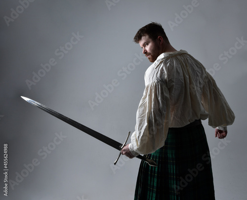 Картината върху платно Close up portrait of handsome brunette man wearing Scottish kilt and renaissance white  pirate blouse shirt