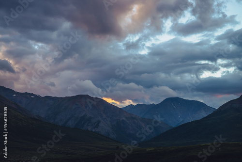 Beautiful mountain scenery with golden dawn light in cloudy sky. Scenic mountain landscape with illuminating color in sunset sky. Silhouettes of mountains on sunrise. Gold illuminating sunlight in sky