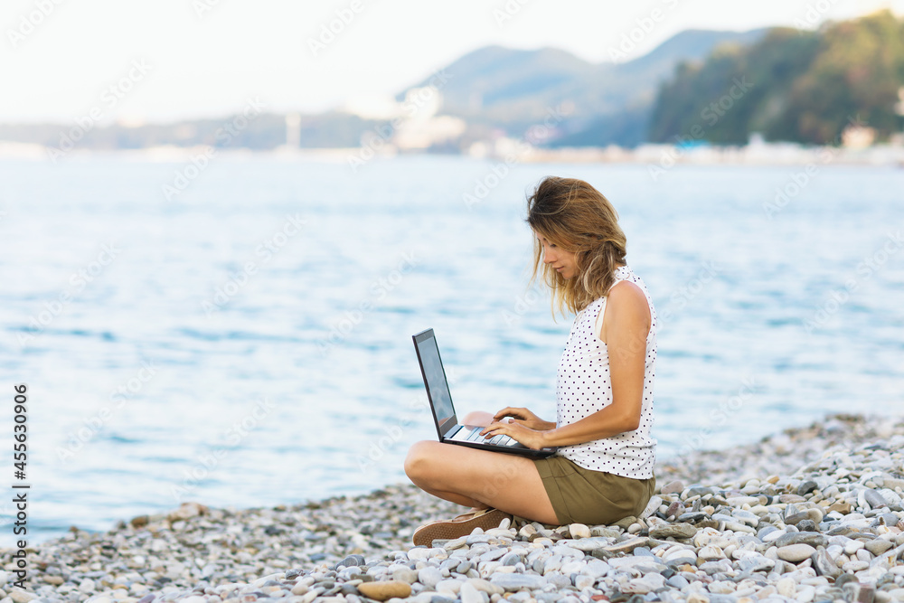 A woman combines remote work at a laptop and a vacation on the seashore
