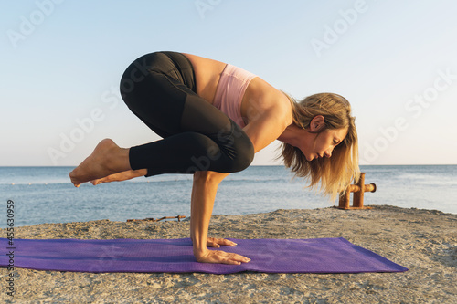 A woman in sportswear practicing yoga on the seashore performs the kakasana exercise, crow pose photo