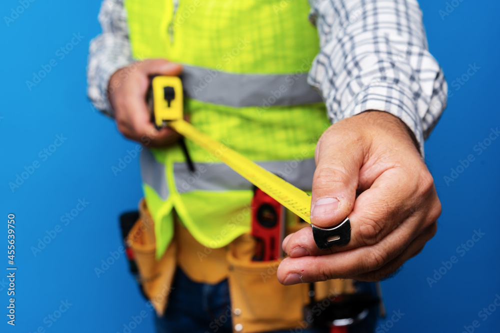 Male builder holding measuring roulette against blue background Male builder holding measuring roulette against blue background