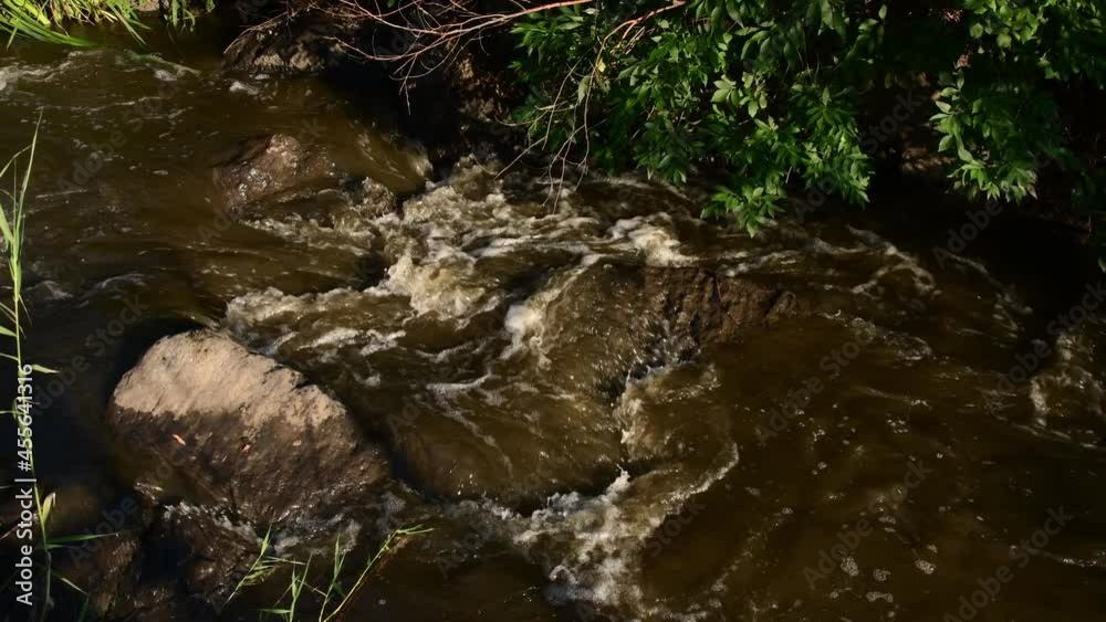 Stream of muddy water flow among granite stone rocks of mountain river full of water after rain. Dirty water cascade flowing through stone rapids. Natural disaster flood background Stream of muddy water flow among granite stone rocks of mountain river full of water after rain. Dirty water cascade flowing through stone rapids. Natural disaster flood background