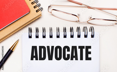 On a light background - glasses in gold frames, a pen, brown and red notepads and a white notebook with the text ADVOCATE. Business concept photo