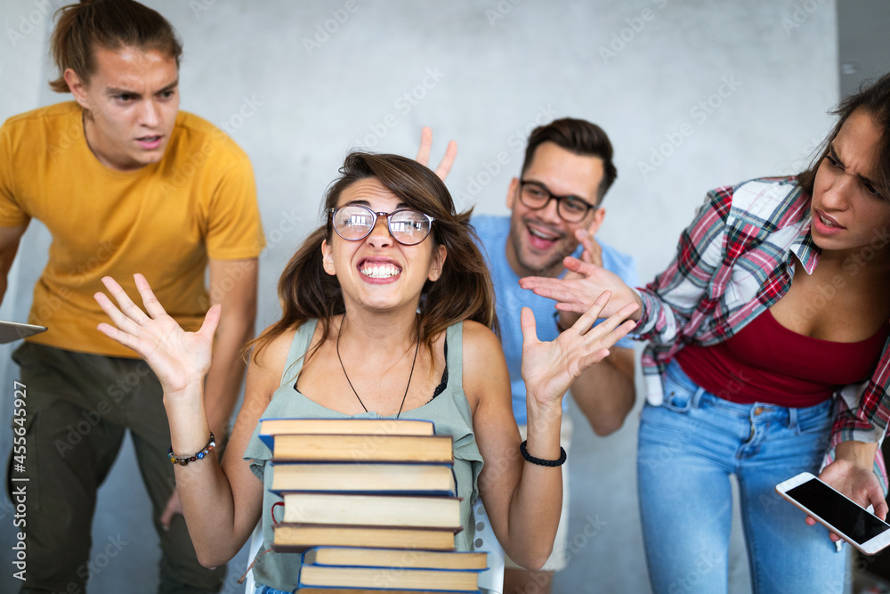 Unhappy student girl looking at her lazy mates who are playing with the phone instead of working Unhappy student girl looking at her lazy mates who are playing with the phone instead of working