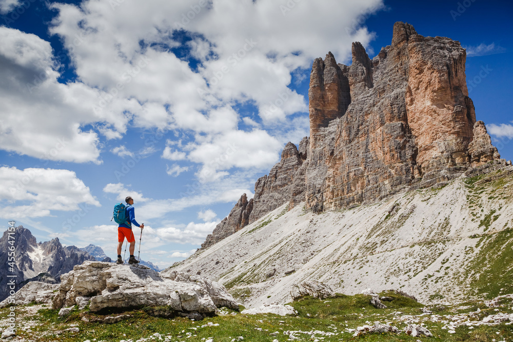 Traveler Man with backpack standing on edge of cliff and looking at the mountains. National Park Tre Cime di Lavaredo, Dolomites Mountains, Italy