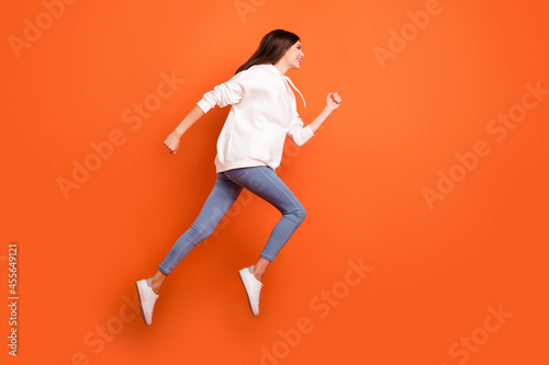 Full length body size profile side view of pretty motivated cheerful girl jumping running isolated bright orange color background © deagreez