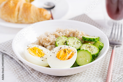 Breakfast oatmeal porridge with boiled egg, cucumber and sesame seed. Healthy balanced food.