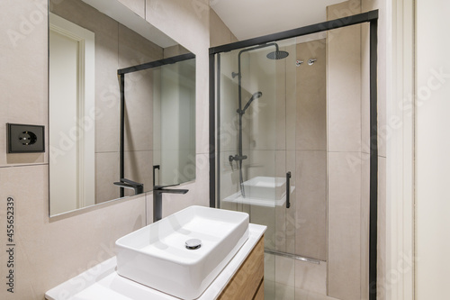 Interior of modern style bathroom in refurbished apartment. Shower zone  sink with black faucet and mirror.