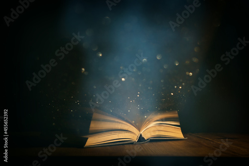 Magical image of open antique book over wooden table with glitter lights