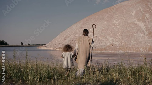 Jesus walks with the girl holding her hand towards the reservoir. High quality 4k footage