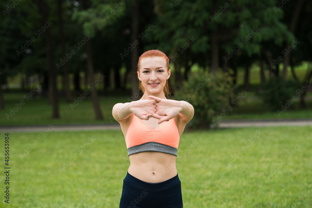 Redhead caucasian woman standing on the grass stretching her arms