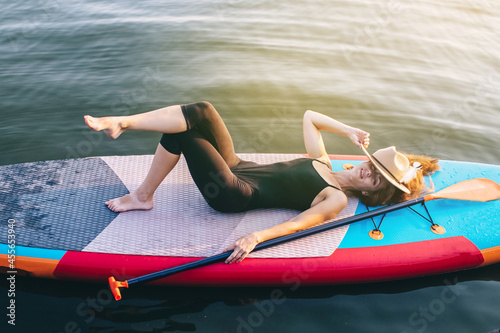 Close-up of a girl floating on a sup board. The concept of water sports, relaxation and self-immersion. Lonely woman alone on a board against a background of water and a pier.