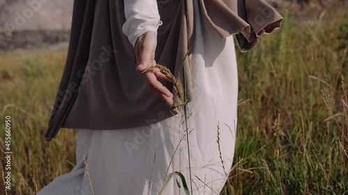 Jesus is walking on the grass, touching the ears with his hands. Close-up. There are traces of a crucifixion on the hands. High quality 4k footage photo