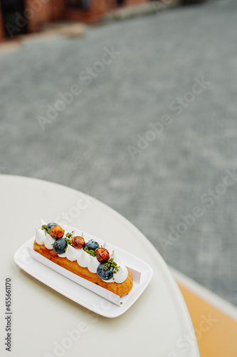 vertical food content, delicious beautiful eclair with white cream, fresh blueberries and caramel on the table of an outdoor cafe. selective focus