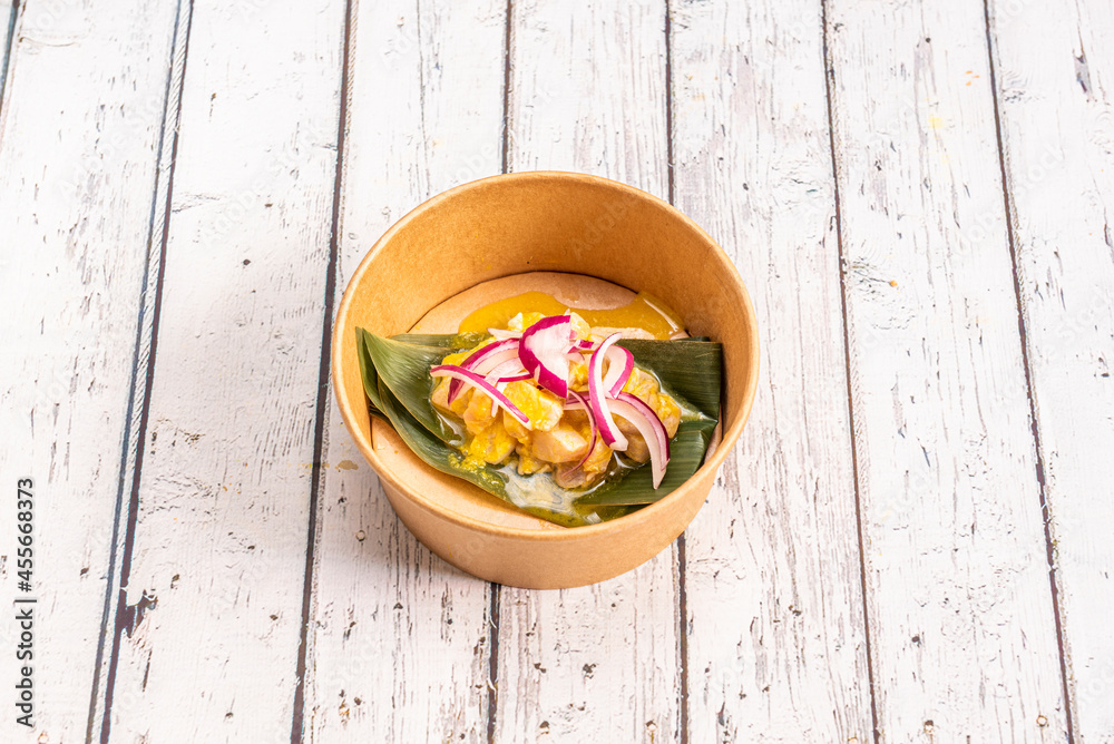 Delicious Peruvian corvina ceviche with purple onion on banana leaf in a take away container