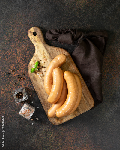Pork sausages on a serving wooden board on a dark culinary background top view