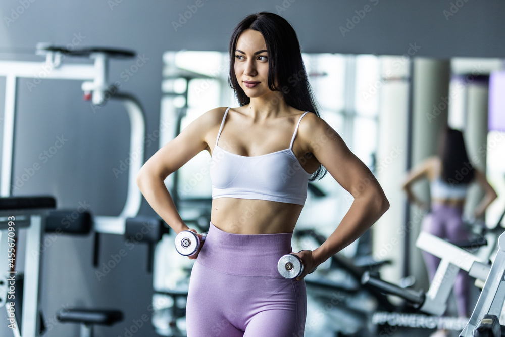 Fototapeta premium Attractive young sporty focused fitness woman doing biceps exercises while sitting on the bench and raising dumbell in the gym