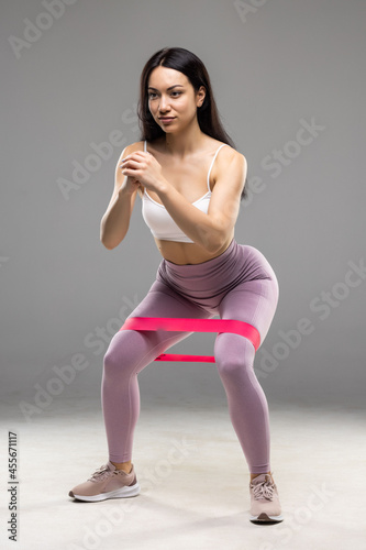 Athletic woman working with resistance band. Portrait of attractive girl with beautiful athletic body on white background.
