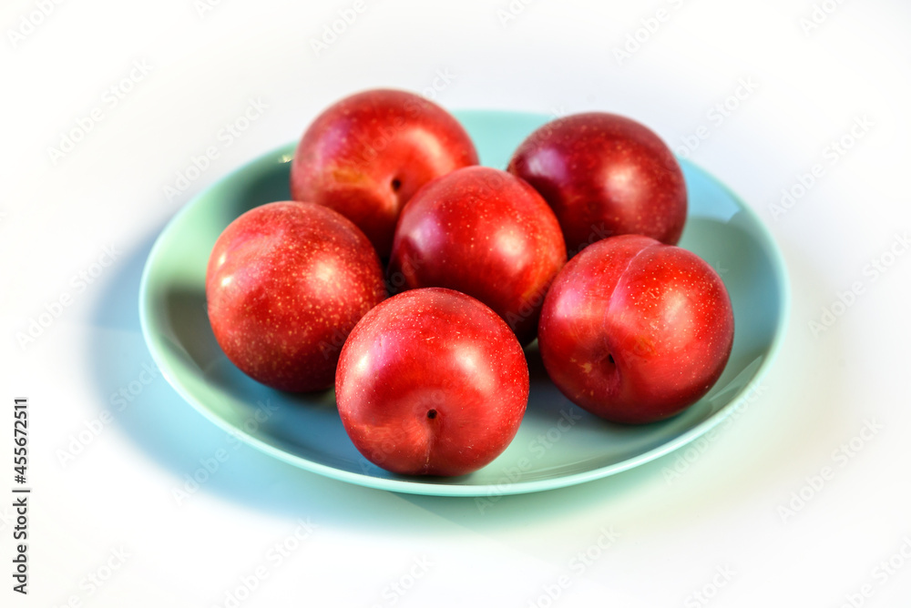 Raw Organic Red Plums on white background, fresh shiny fruits. Farm fresh organic red plums produce in plate on white background Raw Organic Red Plums on white background, fresh shiny fruits. Farm fresh organic red plums produce in plate on white background