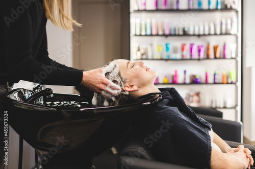 Master woman hairdresser washes hair of a girl with shampoo before styling in a beauty salon.