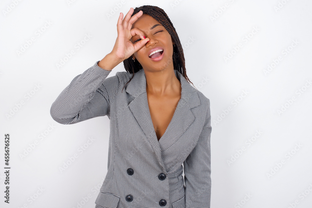 Young african american business woman with braids over white wall with happy face smiling doing ok sign with hand on eye looking through finger. Young african american business woman with braids over white wall with happy face smiling doing ok sign with hand on eye looking through finger.