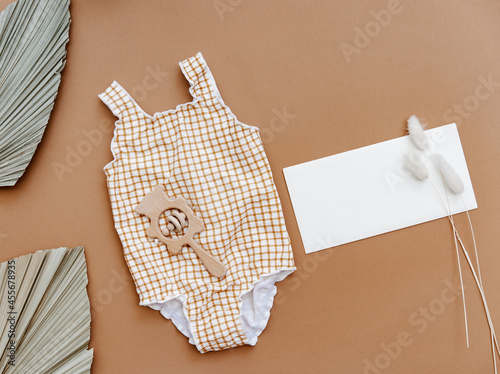 Cute retro swimsuit for baby girl with seashells and beach accessories on brown background. Summer holiday concept. Top view, flat lay photo