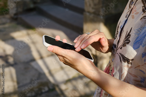 A girl on the street is holding a modern smartphone, sending a text message or using an application on her mobile phone. View city map using smartphone. Smartphone close-up