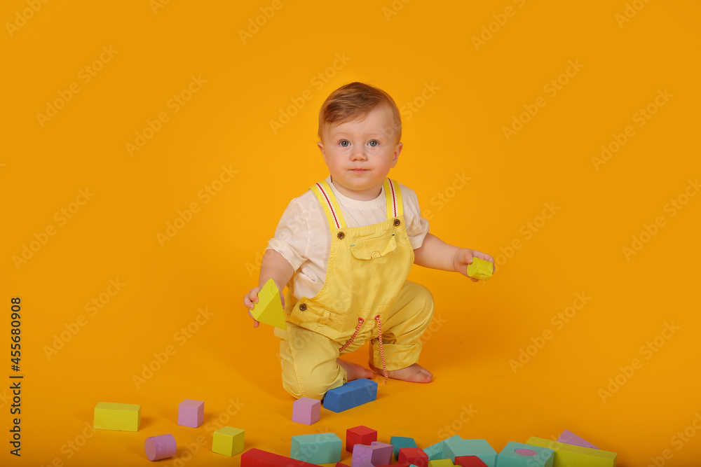 a beautiful blue-eyed little boy in a yellow suit plays with colorful toys a beautiful blue-eyed little boy in a yellow suit plays with colorful toys
