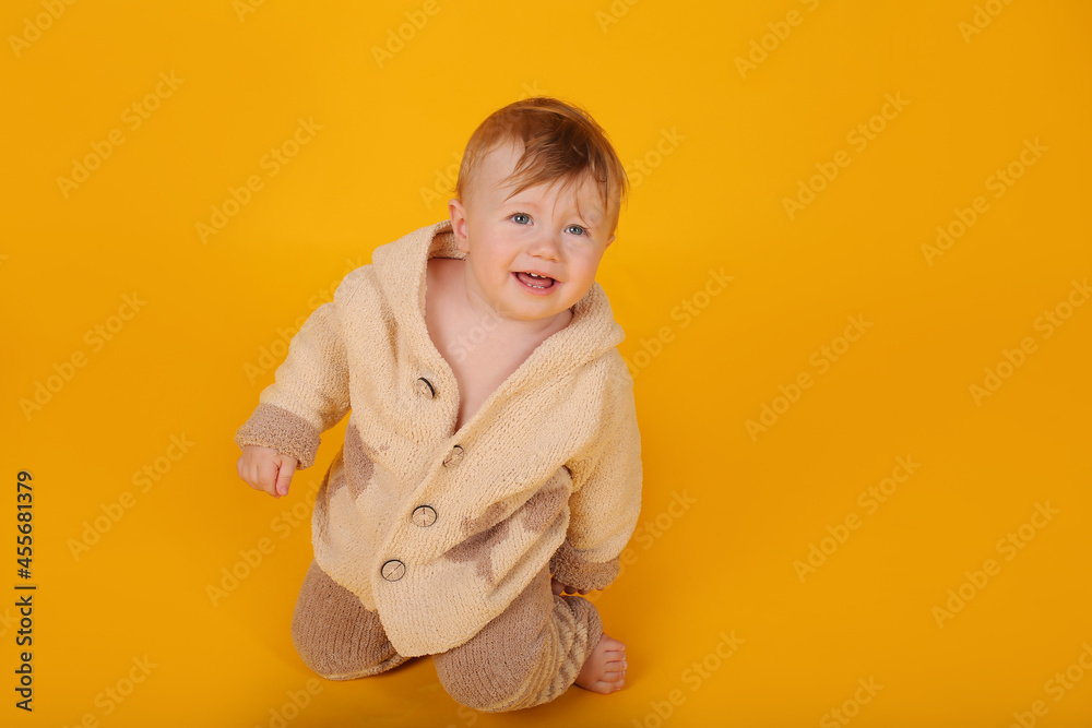 a beautiful blue-eyed baby is sitting on a yellow background in a knitted suit a beautiful blue-eyed baby is sitting on a yellow background in a knitted suit