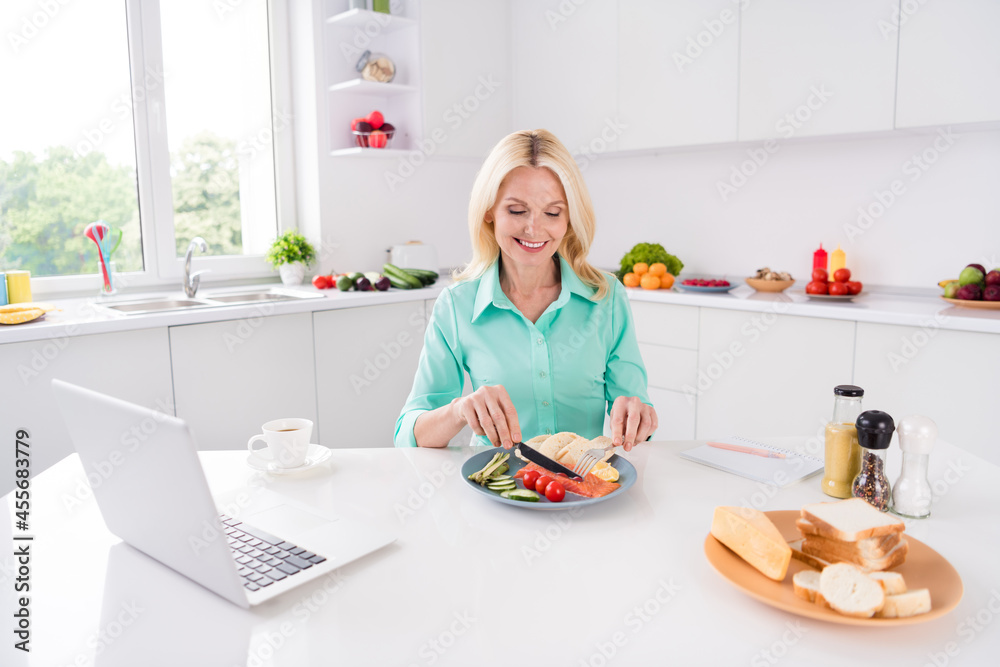 Photo of mature gorgeous nice looking smiling woman grandma eat salmon enjoying tasty meal food at home house kitchen Photo of mature gorgeous nice looking smiling woman grandma eat salmon enjoying tasty meal food at home house kitchen