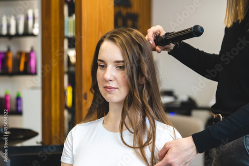 Master woman hairdresser gently curls hair curling girl in a beauty salon. Hair styling