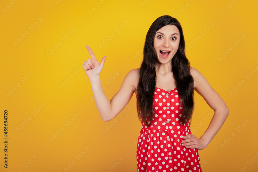Portrait of shocked funny woman finger indicate up empty space open mouth wear dotted red dress on yellow background Portrait of shocked funny woman finger indicate up empty space open mouth wear dotted red dress on yellow background