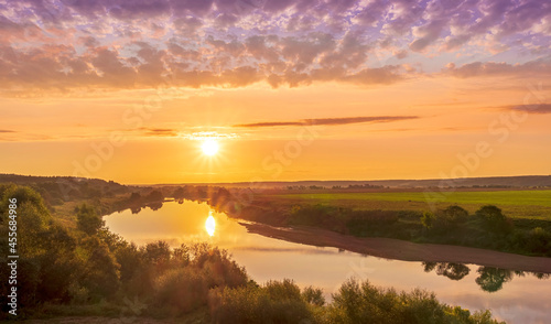 amazing view at beautiful summer river sunset  halo with reflection on water with green bushes  calm water  deep colorful cloudy sky and glow on horizon on a background  spring evening landscape