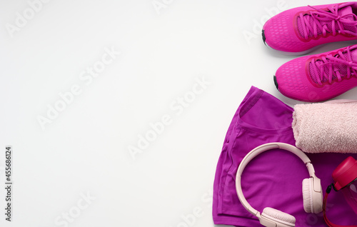a pair of textile purple sports sneakers, wireless headphones, a towel and a bottle of water on a white background. Sportswear